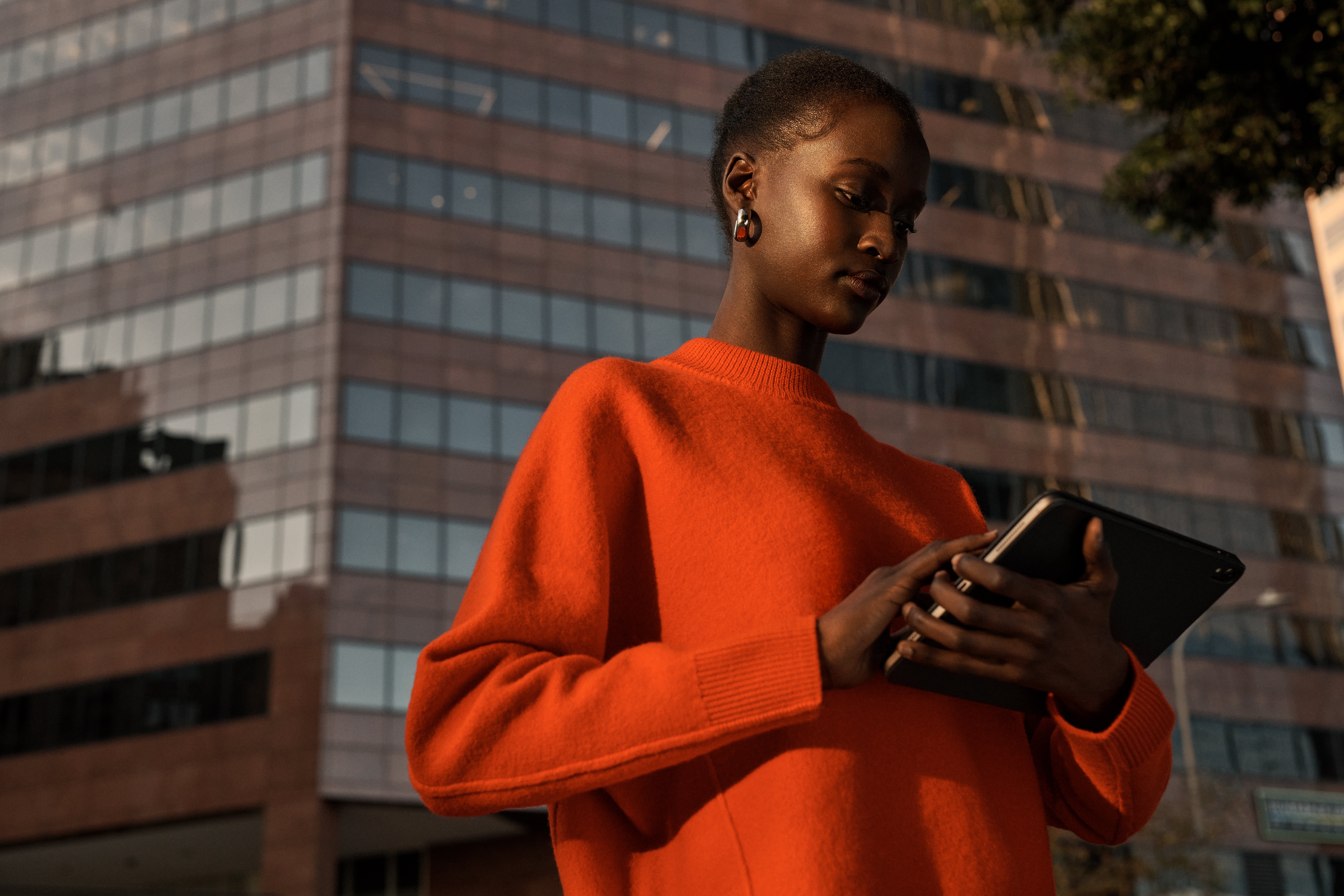 Femme avec iPad et pull orange dans la rue