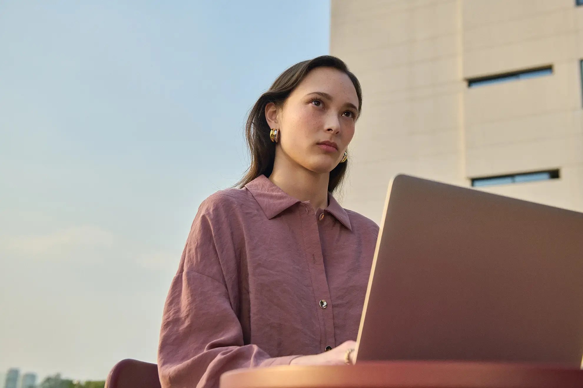 Jeune femme travaillant avec concentration sur un ordinateur portable, à l’extérieur devant un bâtiment moderne